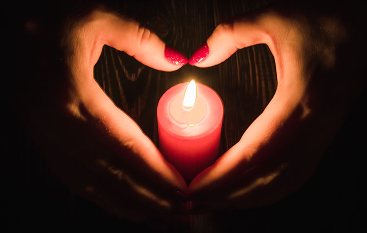 Hands forming a heart shape around a red candle used in love spells to attract romance.
