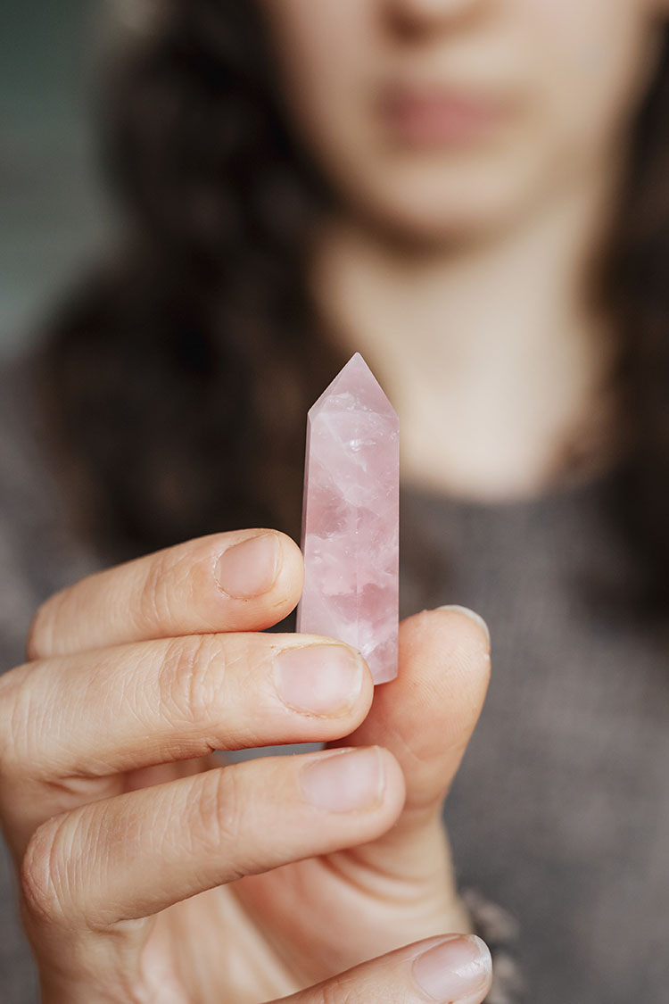 Person holding a rose quartz crystal commonly used in love spells to attract emotional connection.
