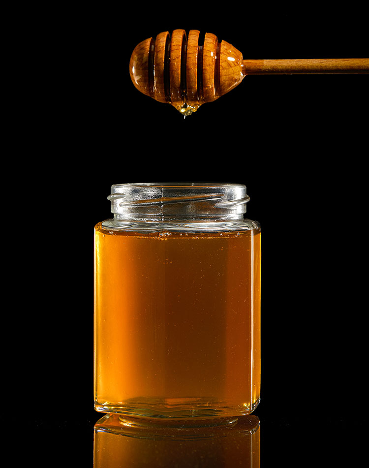 Glass jar of honey with dipper, used in love spells to sweeten romantic intentions.