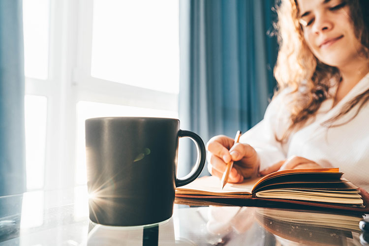 A person journaling their manifesting goals with a cup of coffee.